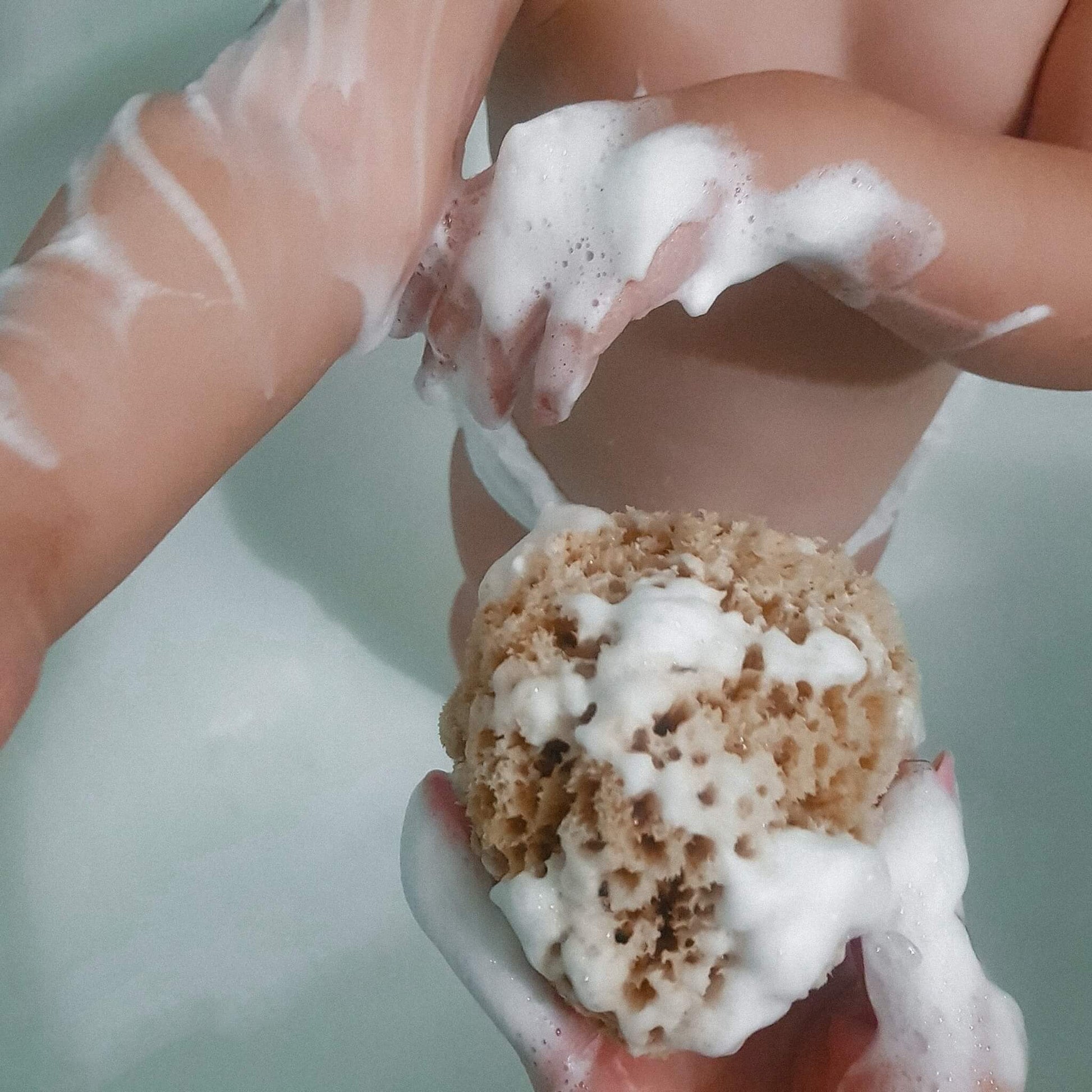 Baby sitzt in der Badewanne und spielt mit einem stark aufgeschäumten Naturschwamm