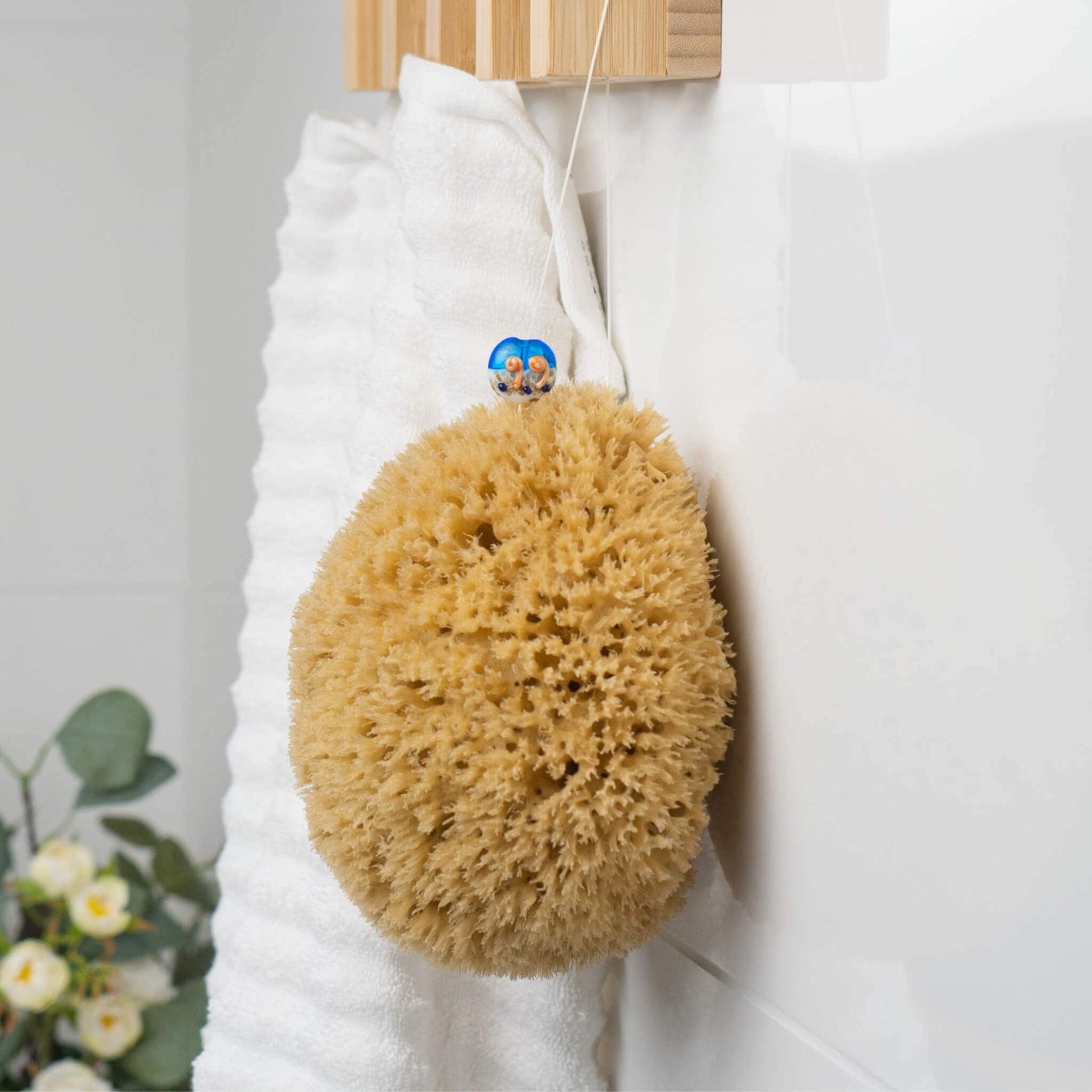 Naturschwamm mit Kordel hängt im Badezimmer neben einem weißen Handtuch