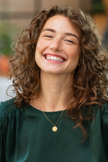 Junge Frau mit lockigem Haar und Sommersprossen, lächelnd und in einem dunkelgrünen Oberteil gekleidet – Kunde von tom&pat Naturprodukte.