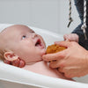 Lachendes Baby in der Badewanne wird sanft mit einem Naturschwamm gewaschen