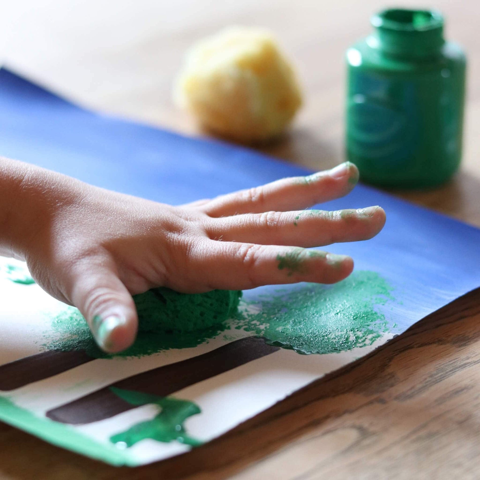 Ein Kind tupft mit einem Naturschwamm in grüner Farbe auf Papier – idealer Malschwamm für Kinder und kreative Bastelideen.