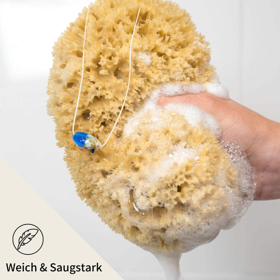 Hand hält schäumenden Naturschwamm mit Kordel – weich, saugstark und ideal zur täglichen Duschpflege